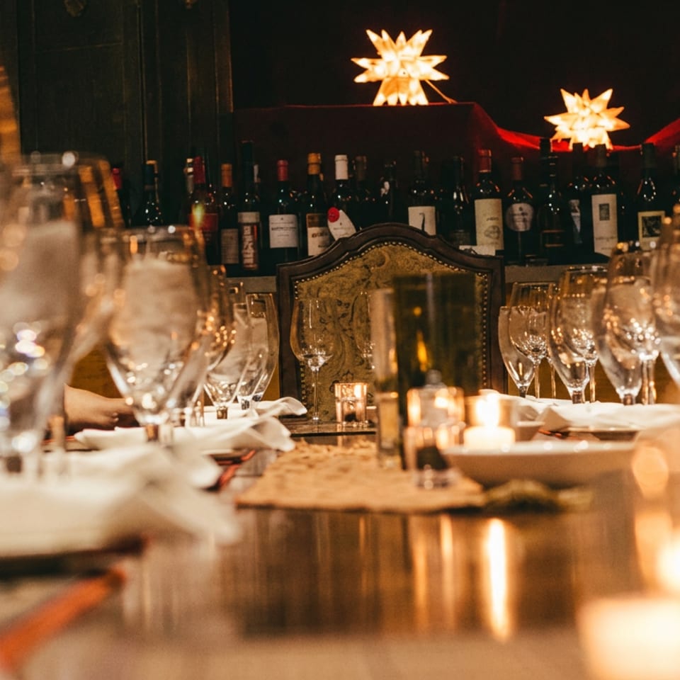 Elegant restaurant dining room with candlelit tables, wine bottles, crystal glassware, and glowing star-shaped lights.
