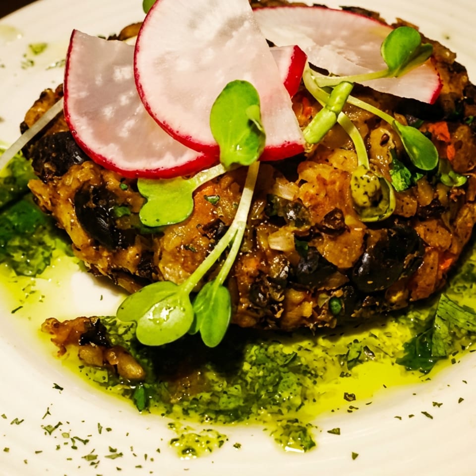 Rustic savory vegetable cake topped with radish slices and microgreens, surrounded by vibrant green herb oil on a white plate.