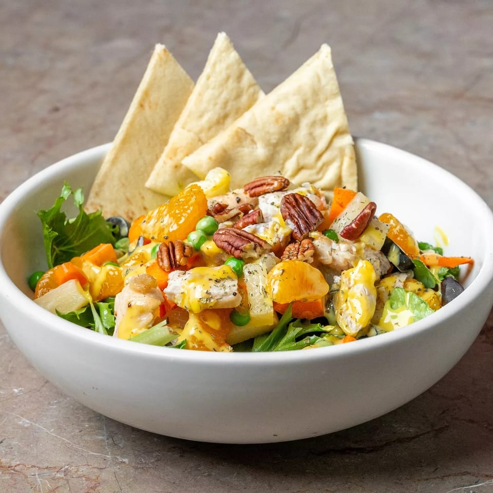 Colorful salad with chicken, vegetables, citrus, pecans, and creamy dressing in a white bowl, served with pita wedges.