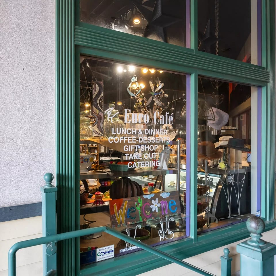 Euro Café storefront with teal framing, window lettering advertising lunch, dinner, coffee, desserts, gifts, takeout, and catering.