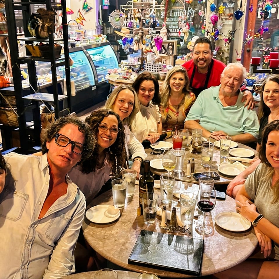 A cheerful group gathers around a restaurant table set with glasses and plates, surrounded by colorful sweets, decorations, and display cases.