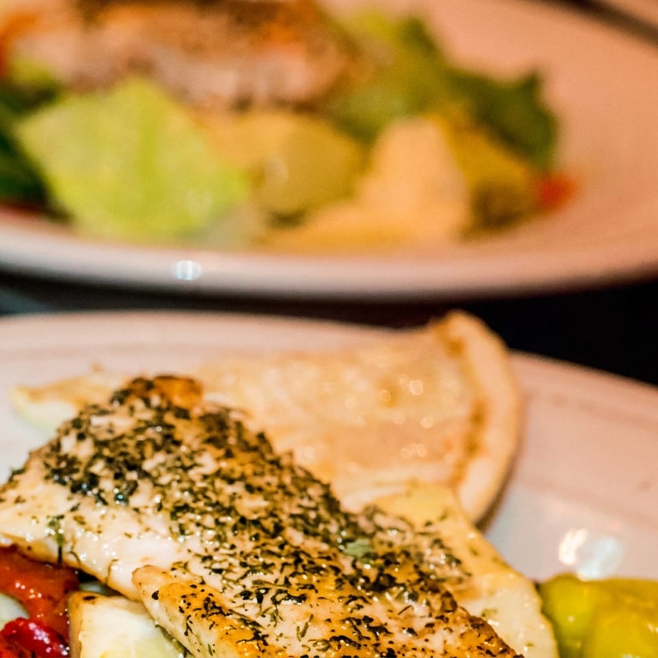 Seasoned grilled chicken with flatbread, leafy salad, roasted tomatoes, and yellow pickles on a plate.
